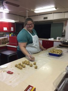 This photograph is of a woman handling food while posing for a picture, conveying our vision of training children in culinary arts.